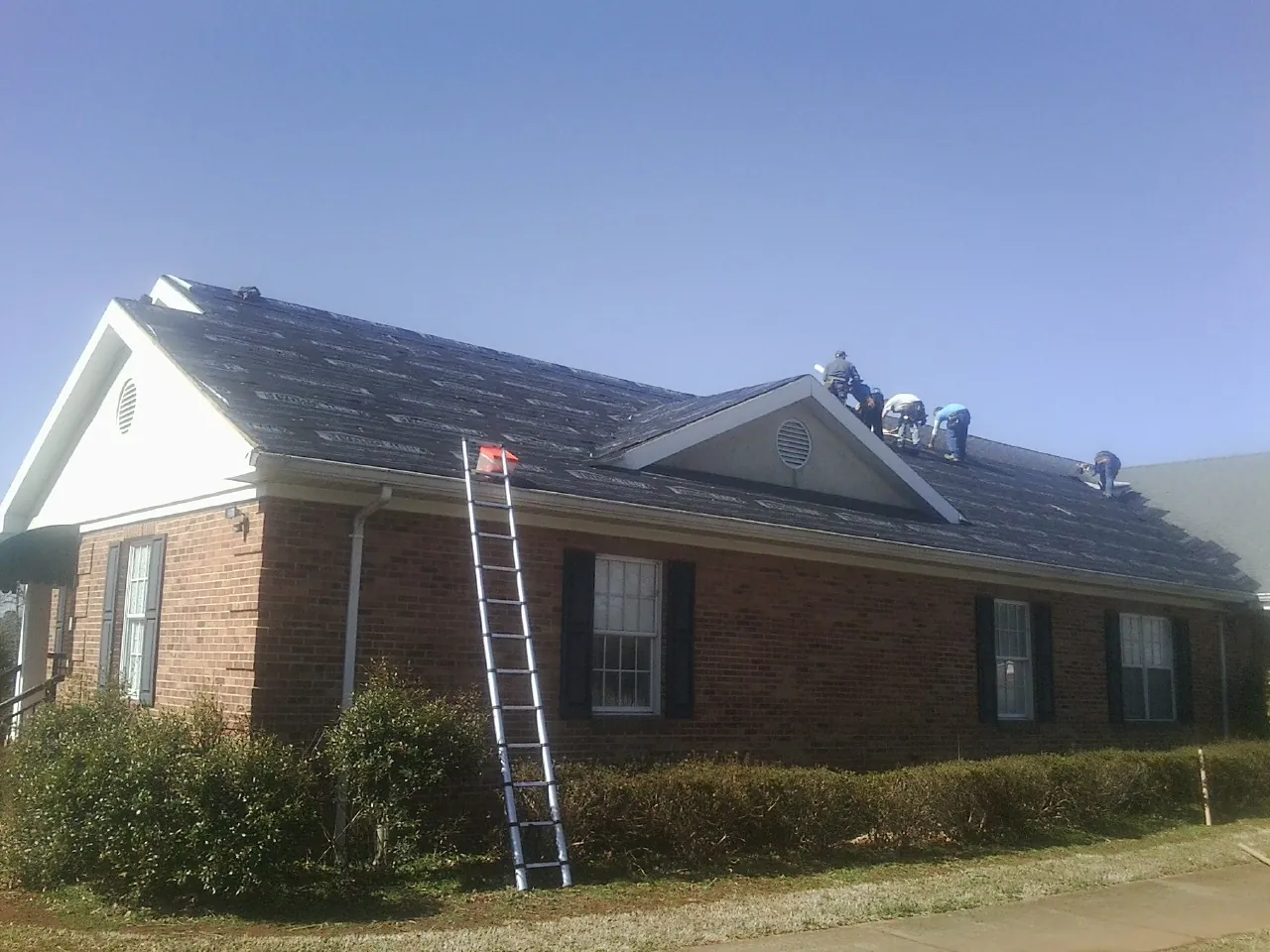 Crew tearing shingles off a brick ranch roof with a ladder set — Metal Roof Repair work by our crew in Tappan