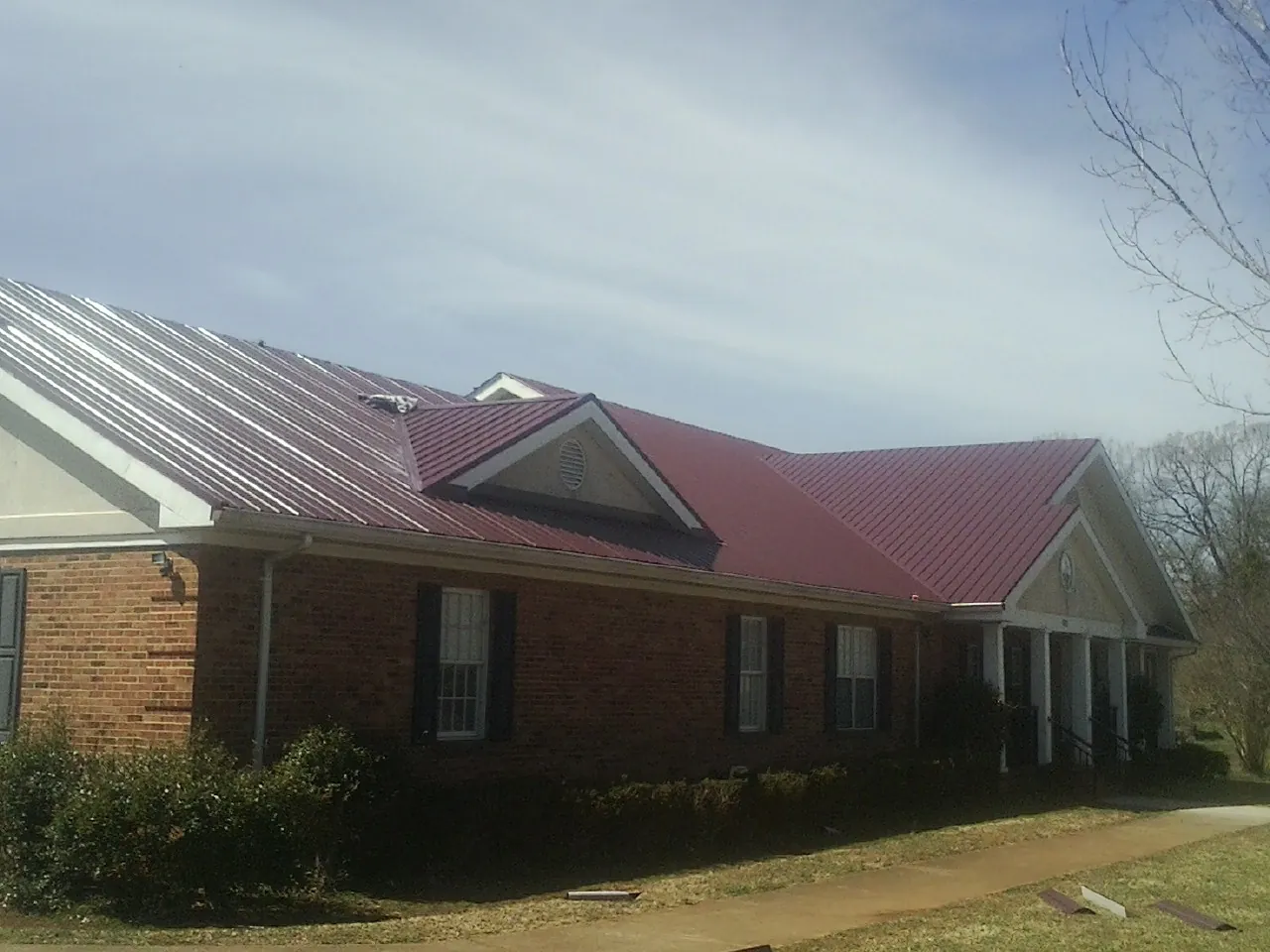 Red metal roof with gabled entries on a long brick building, from a Hail Damage Roof Repair job in Tappan