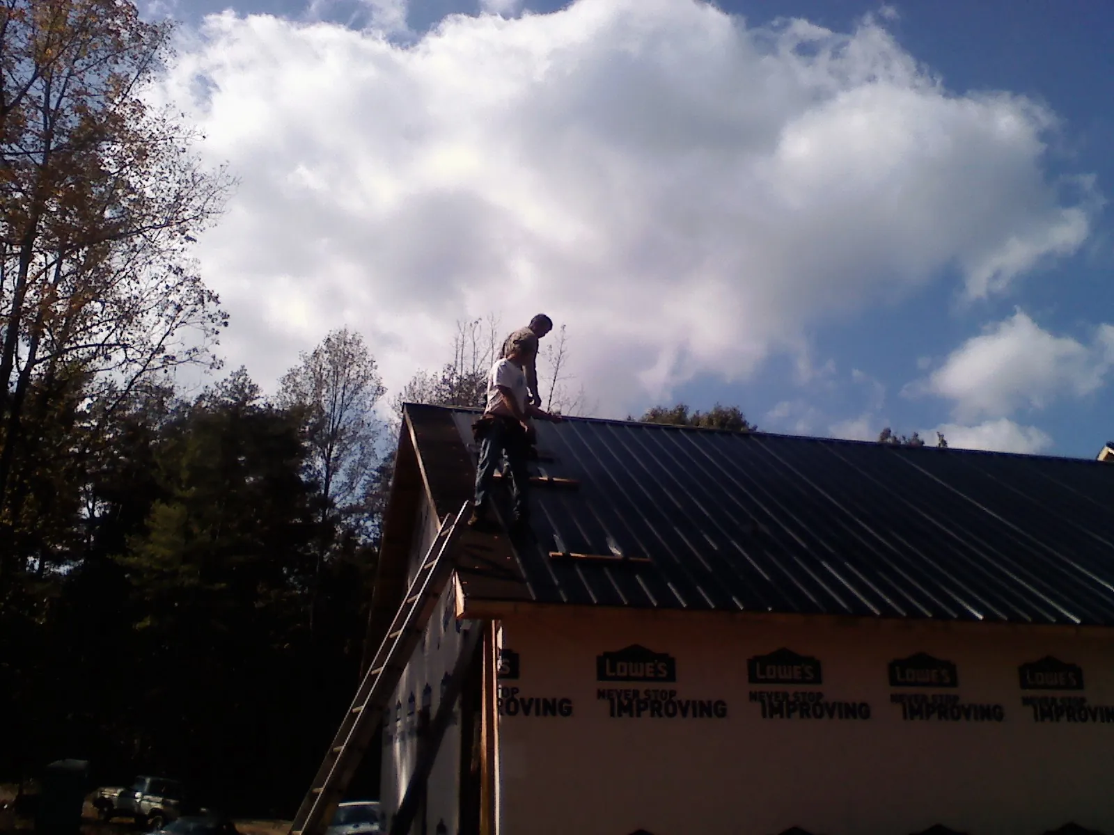 Roofer fastening dark metal panels high against a cloudy sky, from a Roof Inspection job in Tappan