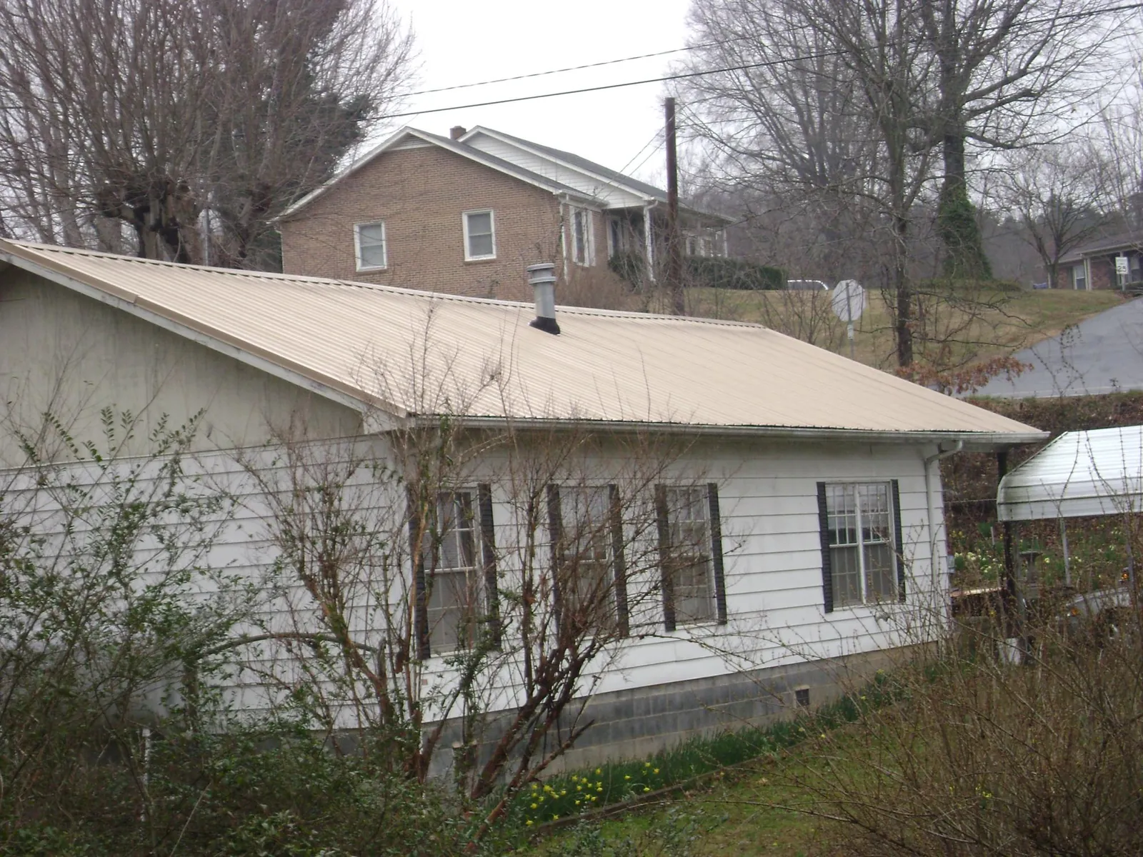 Tan metal roof on a white sided house set into a hillside — Commercial Roofing by Roofing Brothers in Tappan